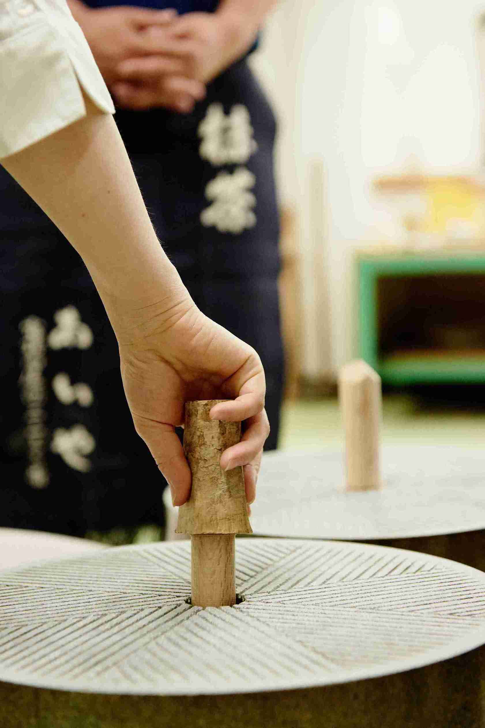 a man holding a wooden piece of a matcha grinder