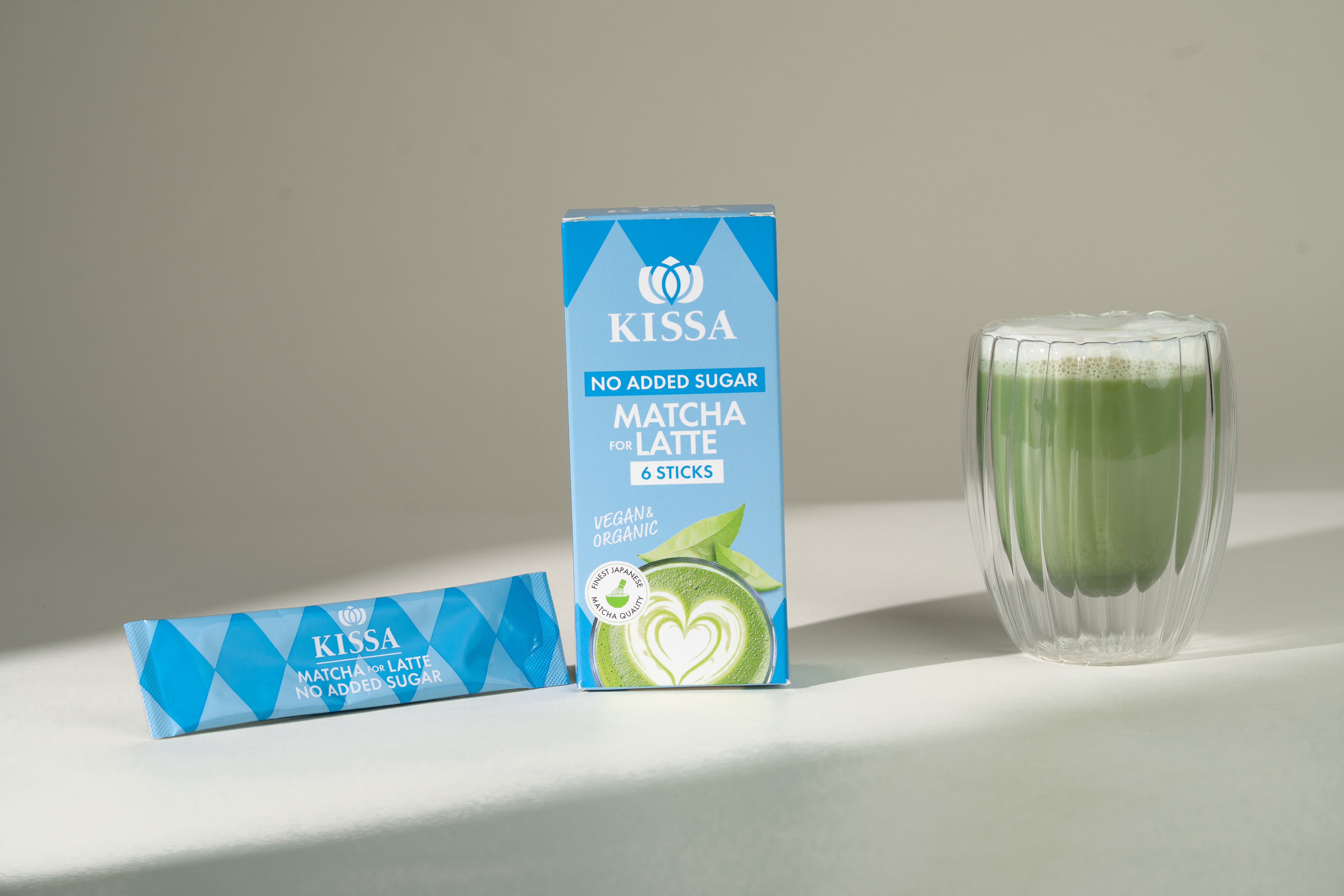 KISSA Matcha Latte Sticks ohne Zuckerzusatz in Box neben cremigem Matcha Latte auf hellem Hintergrund – ideal für zuckerfreien Genuss