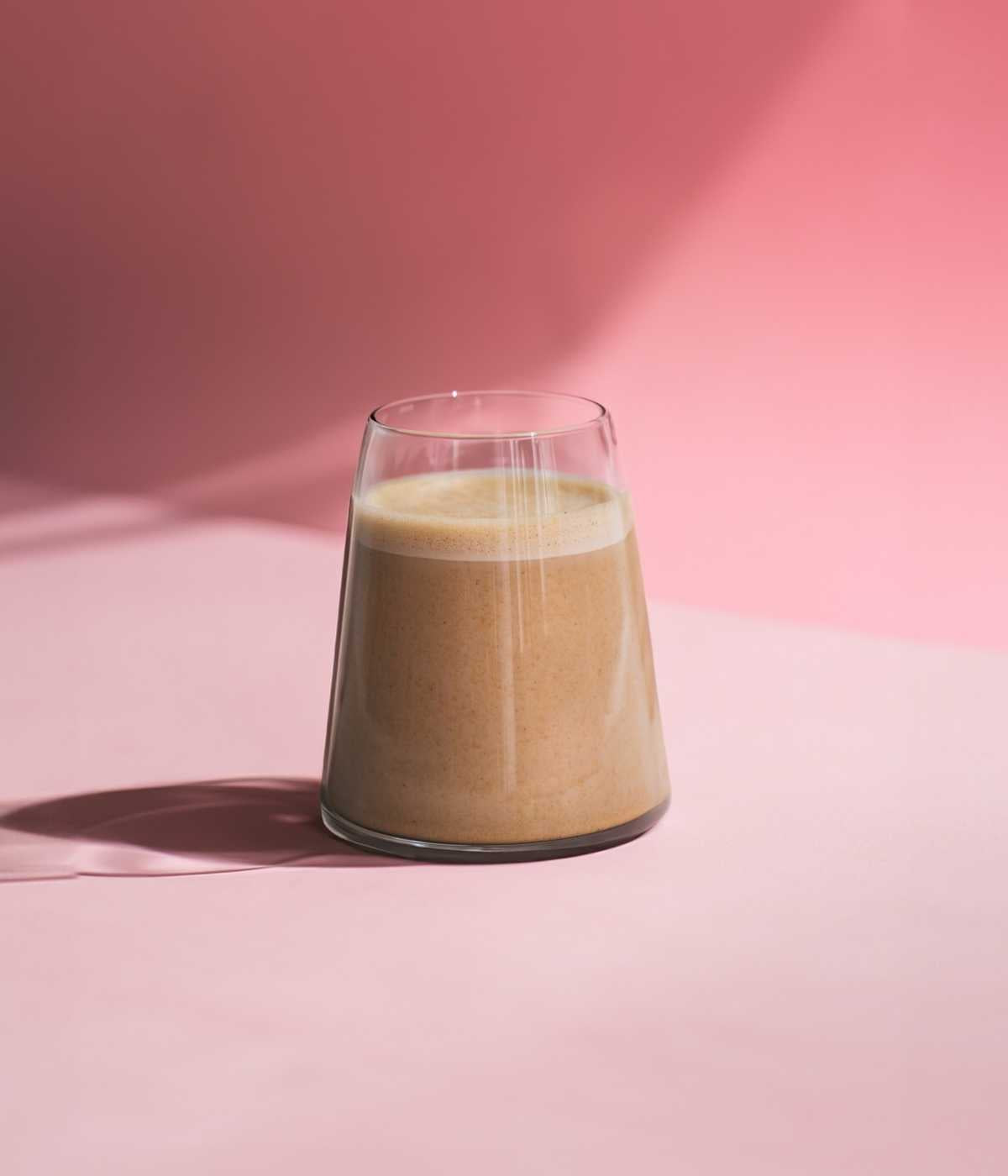 Chai-Latte im Glas vor stilvollem rosa Hintergrund.