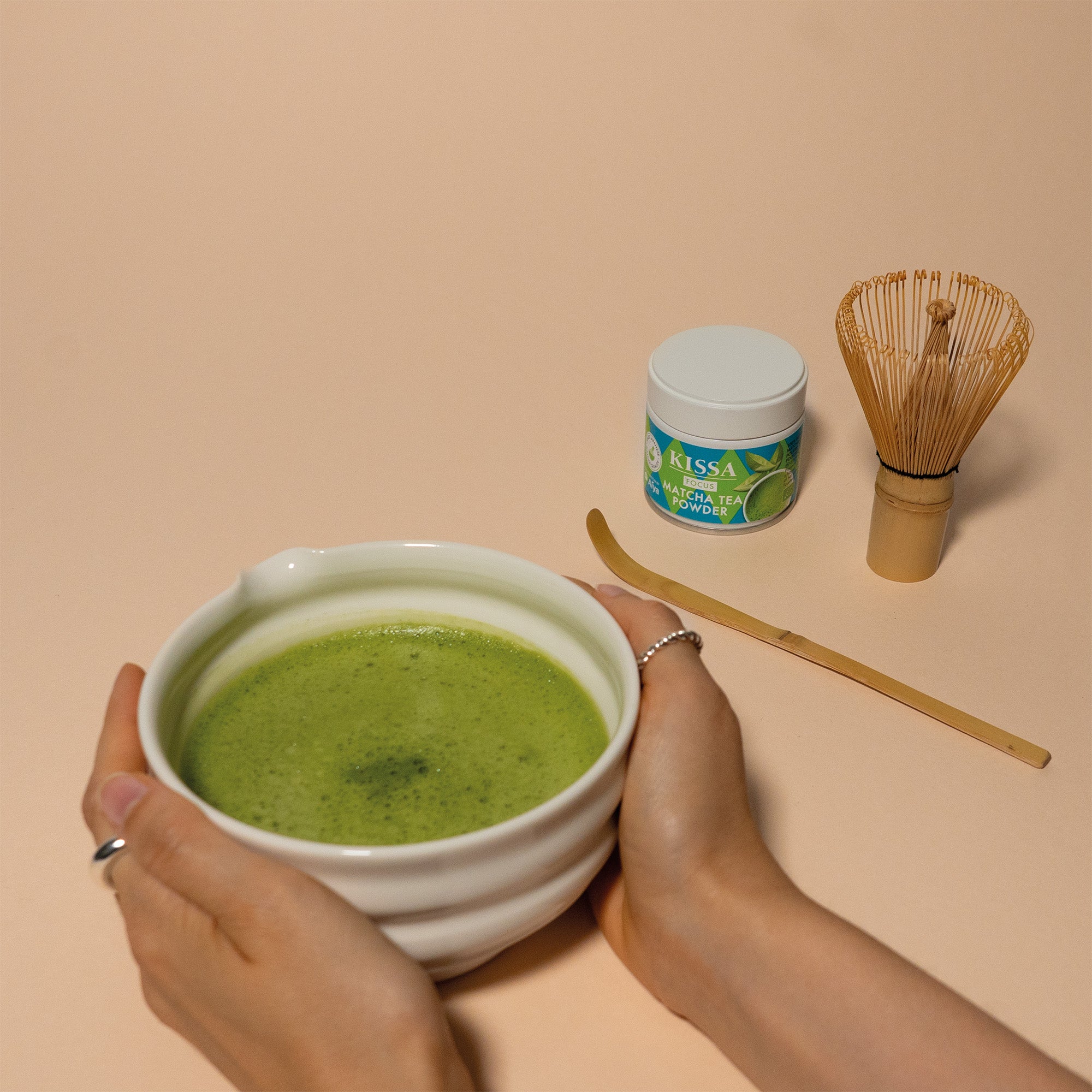 Hands holding a bowl with Matcha, KISSA Matcha Focus tin, Bamboo Whisk and Bamboo Spoon