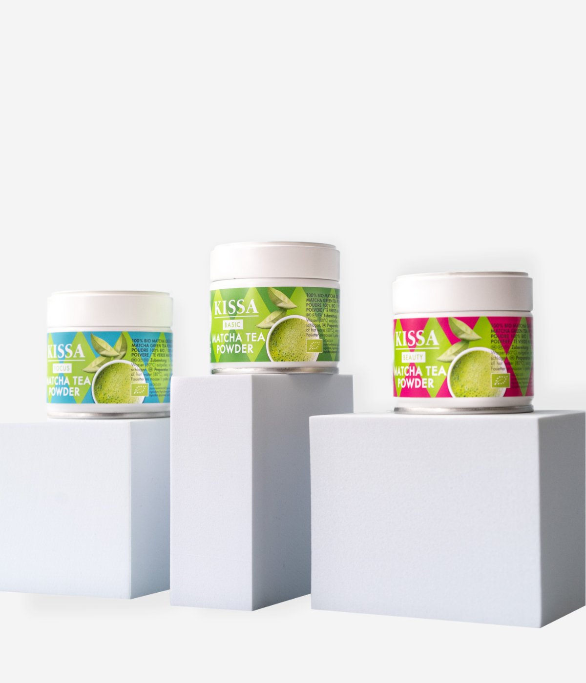 Drei KISSA Pure Matcha-Produkte (Basic, Beauty, Focus) nebeneinander auf hellen Blöcken arrangiert vor hellem Hintergrund.