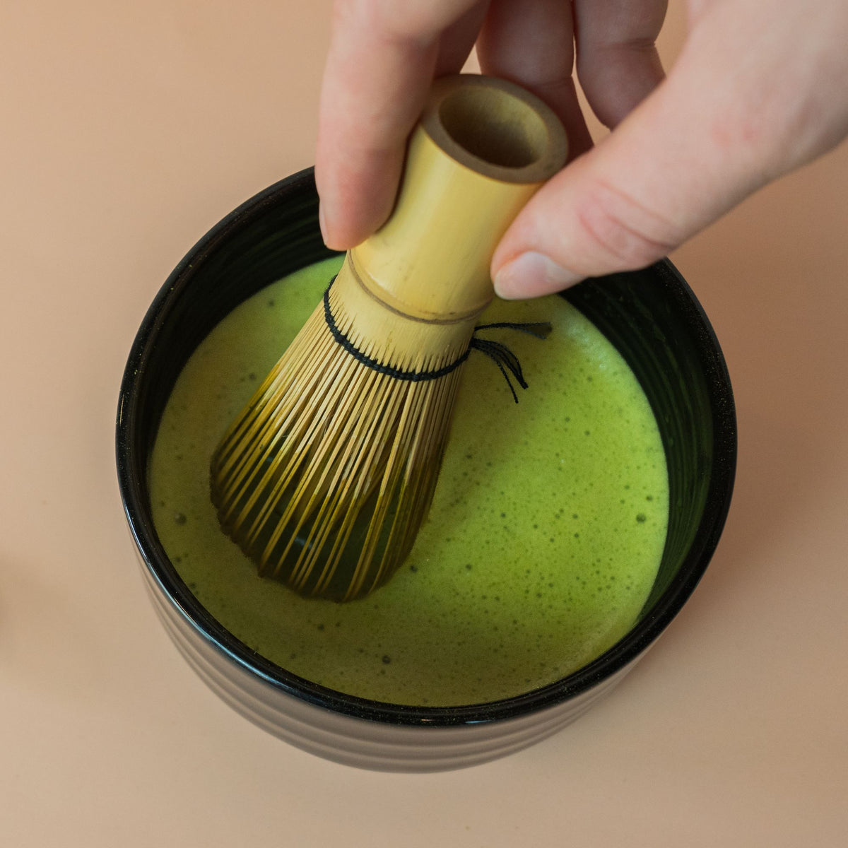 Grüner purer Matcha wird mit einem Bambusbesen in der Schwarzen Miyabi Matcha Bowl schaumig geschlagen