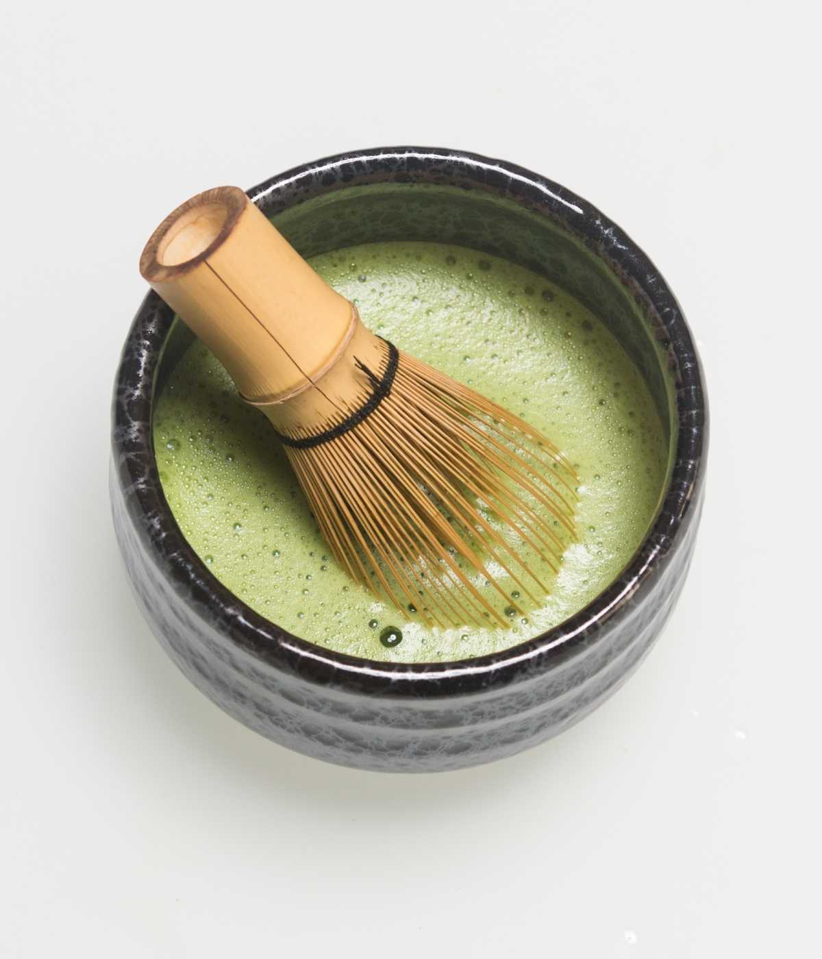 Matcha-Besen steckt in einer halbgefüllten Matcha-Schale mit cremigem, schaumigem Matcha.