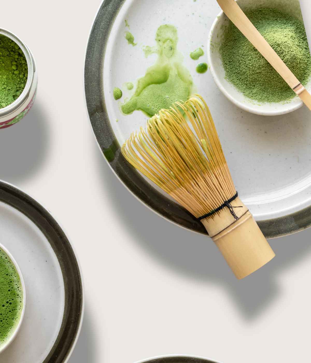 Matcha-Besen liegt auf einem Teller neben einer Portion leuchtend grünen Matcha-Pulvers.