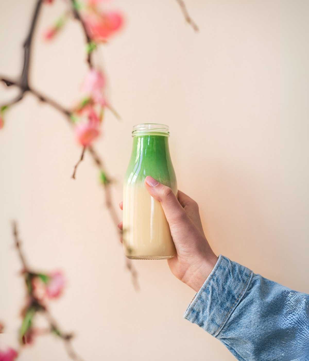 Person hält eine Flasche cremigen Matcha Latte vor rosa Hintergrund