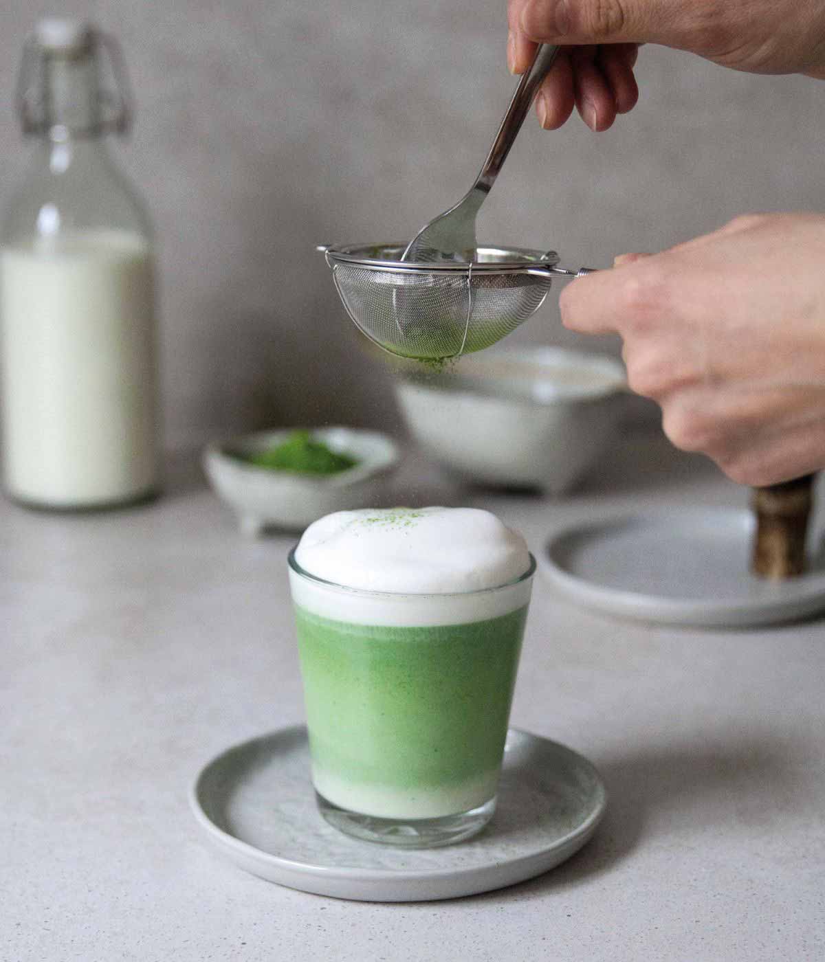 Matcha-Sieb hält feines Pulver über einer Schale Matcha-Latte und streut das Pulver gleichmäßig hinein.