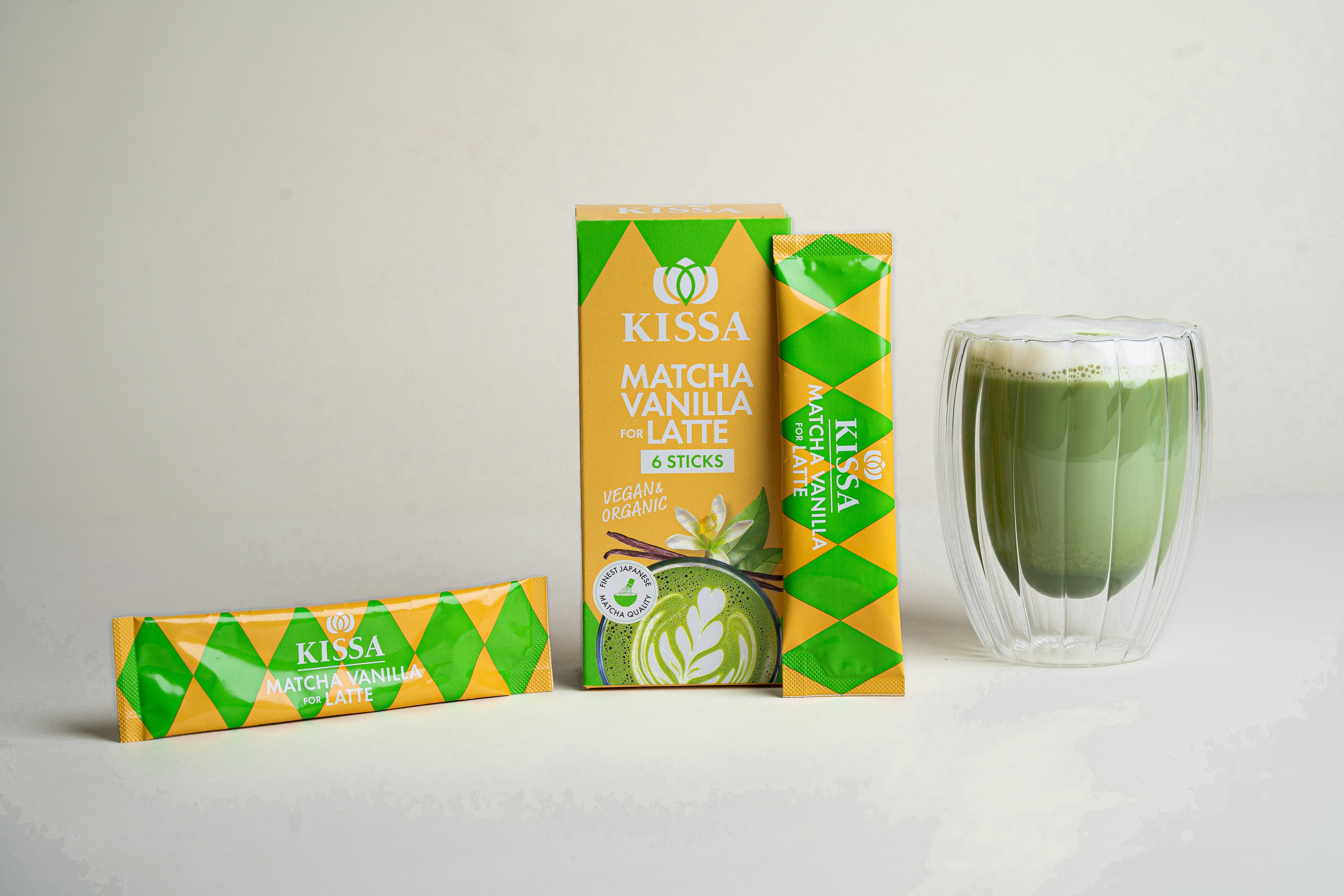 KISSA Matcha Vanilla Latte Sticks in stilvoller Box neben cremigem Matcha Latte auf hellem Hintergrund