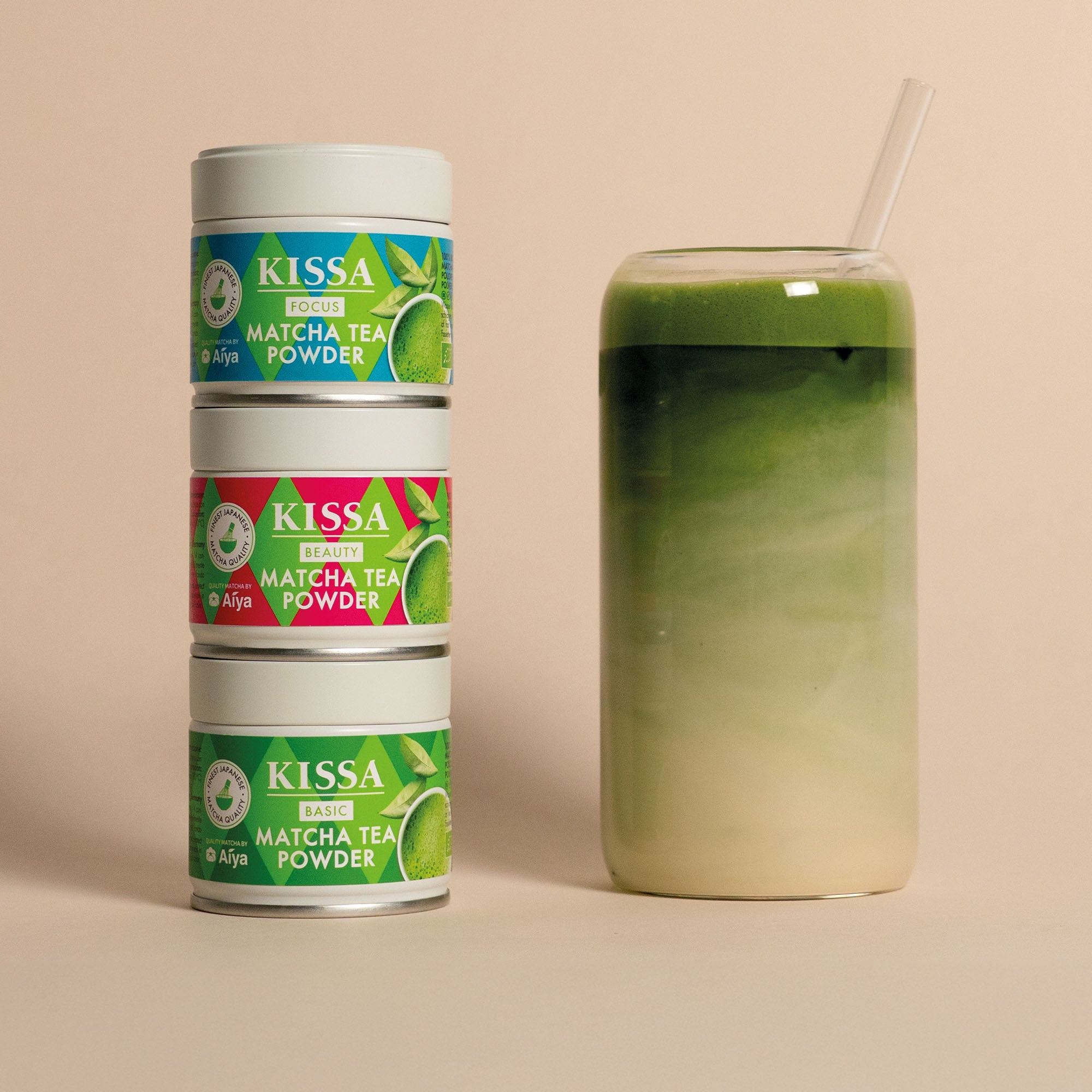 3 pure Dosen KISSA Matcha gestapelt neben einem Glas Matcha Latte